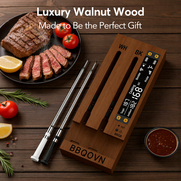 A wooden dual-zone BBQ oven with a digital temperature display and two metal probes, arranged on a dark wood tabletop with steak, tomatoes, lemon, herbs, and sauce. Text at the top reads 'Luxury Walnut Wood Made to Be the Perfect Gift.